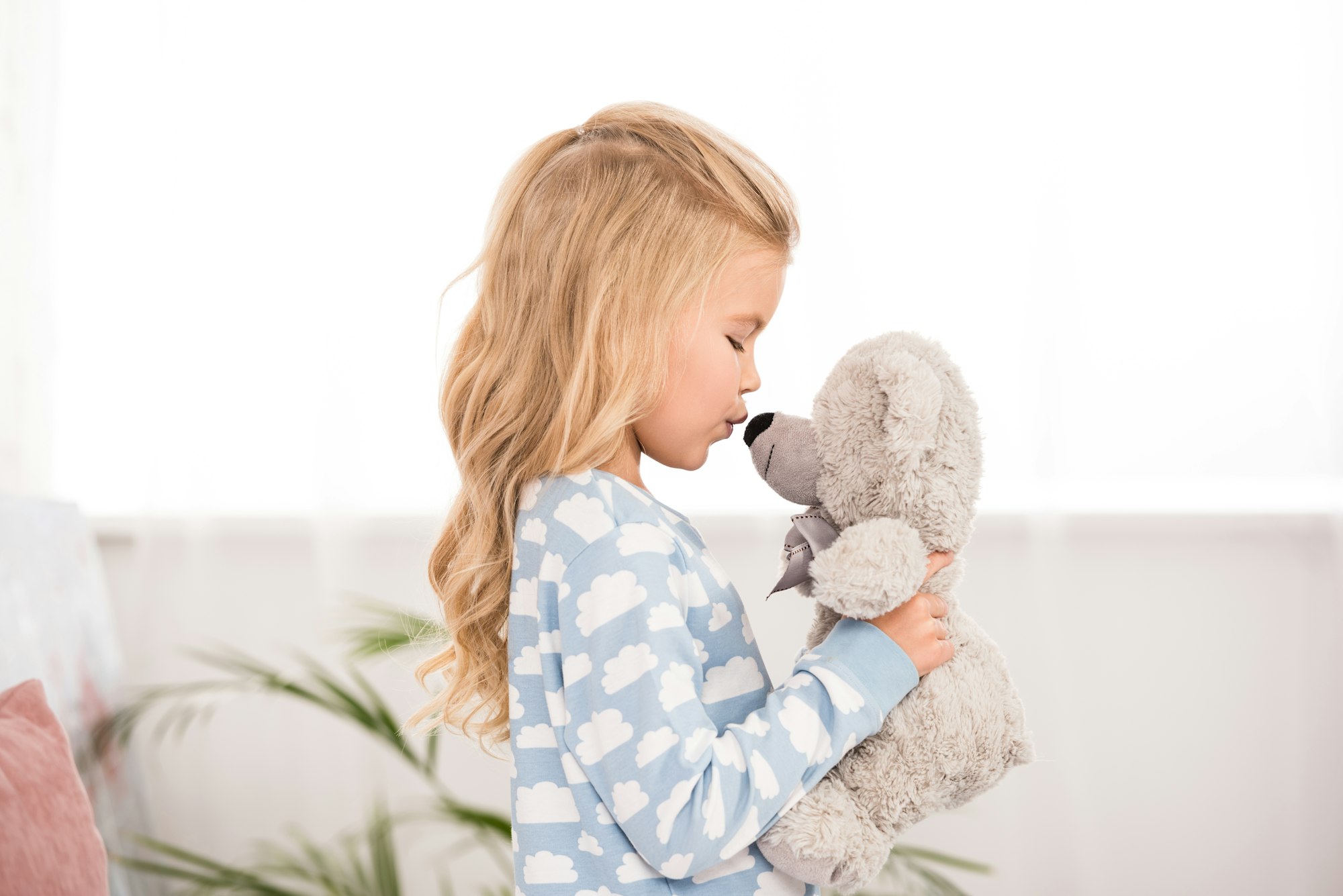 side view of cute kid in pajamas kissing teddy bear